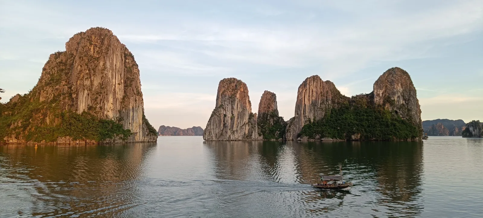 Limestone karsts of Ha Long Bay in evening light with a small boat crossing